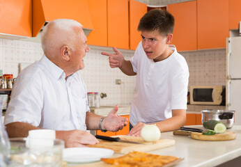 Happy elderly man and his grandson making dinner together in kitchen