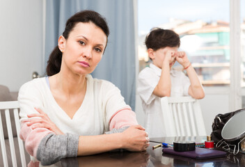 Upset woman sitting and looking away after quarrel with her teenage son..