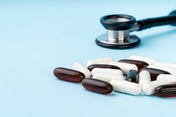 Assorted brown and white capsules, stethoscope, pills, isolated on blue background. Nutritional supplements for weight loss and energy, dietary aids. Health care concept. Copy space, banner