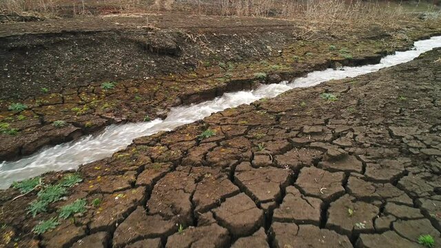 Aerial view of a deeply cracked ground and a small stream. Shot. Concept of dry climate, ecology, and desert invasion.