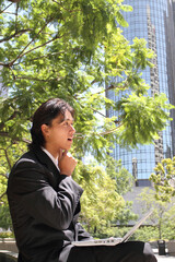 A young Japanese businessman thinking while using a personal computer in a business district in Los Angeles, USA