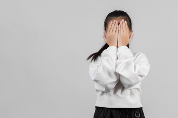 Cute little girl on gray background covering eyes with hands and doing stop gesture with sad and fear expression. Embarrassed and negative
