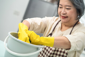 Asian senior woman twisting wet rag in water bucket for house cleaning