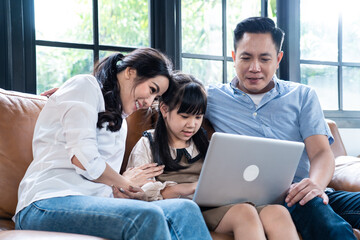 Asian family teaching their daughter to use laptop computer at home.