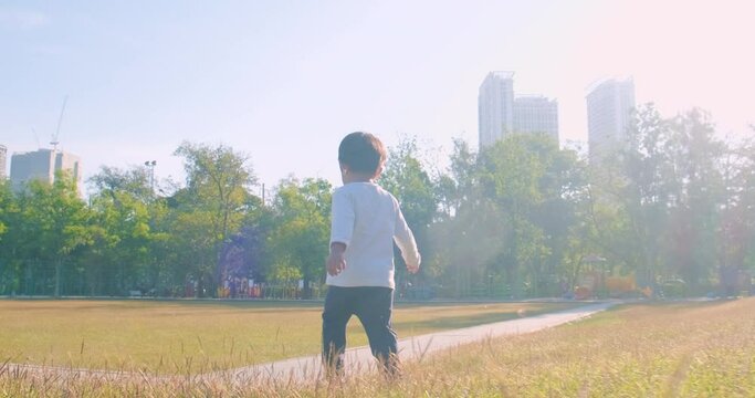 Happy little boy running on green meadow grass morning sunrise in public park