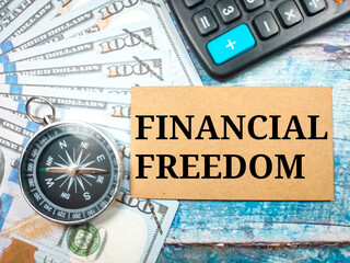 Business concept.Text FINANCIAL FREEDOM with compass, banknote and calculator on wooden background.