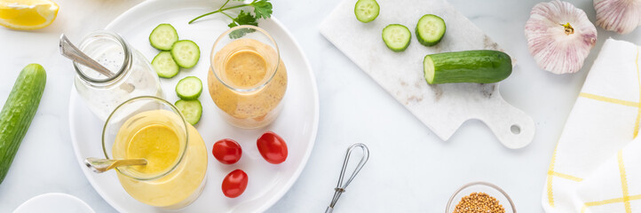 Top down narrow view of three different salad dressings on a small tray surrounded by ingredients to make salad.