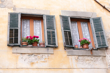 Fototapeta na wymiar Old windows in a medieval town. Windows with street sills with flowers on them. The old Italian shutters are open. Windows in Tuscany in Barga.