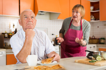 Senior woman scolding her offended husband in kitchen