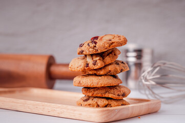 Piles of delicious chocolate chip cookies on a white plate with a milk bottle. Pastry utensils with white linen napkins on a wooden table. Delicious on a white plate with a bottle of milk.