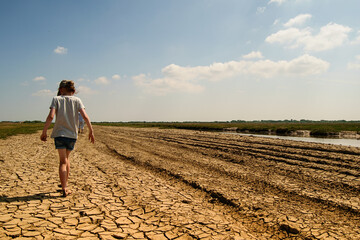Cracked ground in hot sunny day and a small girl walking along the path.