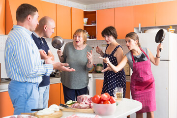 Three women holding frying pans opposing two men in kitchen