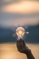 hand holding light bulb against nature, icons energy sources for renewable,
