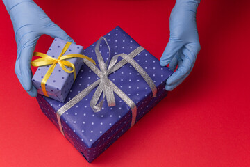 Hands in blue latex gloves holds blue gift boxes in paper with polka dots with tied ribbon with as...