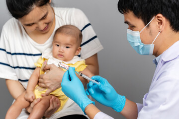 doctor with mask draws coronavirus (covid-19) vaccine out of vial and mother holding baby