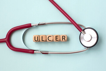 The word ulcer is written on wooben cubes and a stethoscope. Medical concept