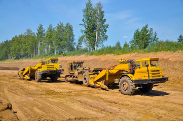 Obraz premium the tractor loads the soil into the dump truck. Construction of a new road.