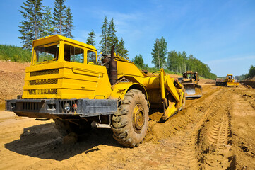 Obraz premium the tractor scraper levels the ground of the new road.