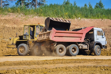 Obraz premium the tractor loads the soil into the dump truck. Construction of a new road.