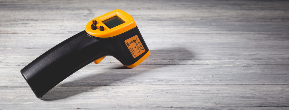 Yellow-black pyrometer on a wooden background. A device for non-contact temperature measurement.