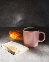 Pink cup witharabica coffee, Quran book and croissant on a dark backgraund