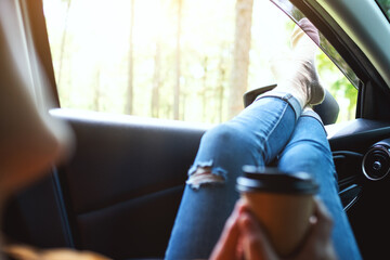 Closeup image of a woman drinking coffee while laying and putting feet and legs outside the car window