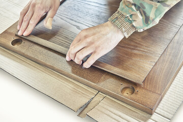 Skilled carpenter assembles wooden door for kitchen cabinet fixing glazing bead on cardboard closeup