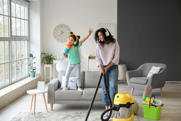 Mother and daughter having fun while hoovering floor in flat