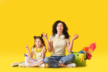 Mother and daughter with cleaning supplies on color background