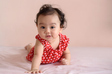 Fototapeta premium Little Asian baby, a cute toddler dressed in red practicing crawling on the bed and looking at the camera