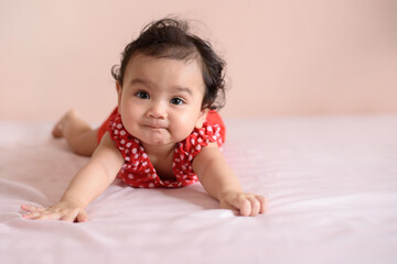 Fototapeta premium Little Asian baby, a cute toddler dressed in red practicing crawling on the bed and looking at the camera