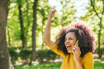Pretty afro woman talking on the mobile celebrating something.