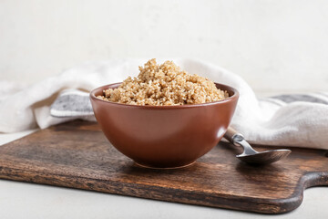 Bowl with tasty quinoa and spoon on light background