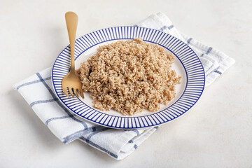 Plate with tasty quinoa and fork on light background