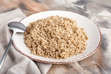 Plate with tasty quinoa and spoon on marble background