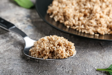 Plate with tasty quinoa and spoon on grey background, closeup