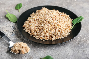 Plate with tasty quinoa and spoon on grey background