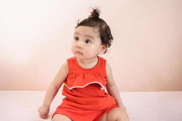 Portrait of a cute little Asian baby girl wear red dress siting and looking out isolated on background, baby expression concept