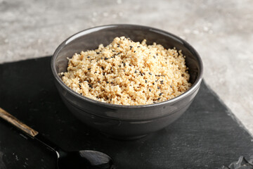 Bowl with tasty quinoa and spoon on grey background, closeup