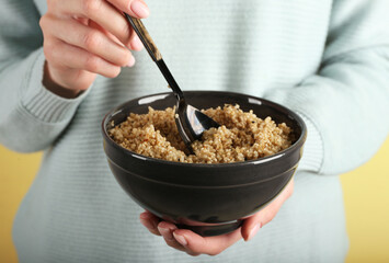 Woman holding bowl with tasty quinoa on color background, closeup