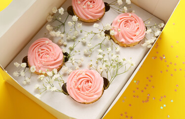 Box with tasty cupcakes and flowers on color background, closeup