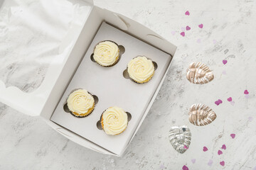 Box with tasty cupcakes and decor on light background