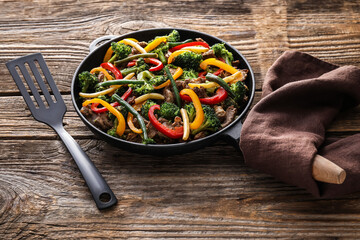 Frying pan with tasty beef and vegetables on wooden background