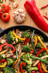 Frying pan with tasty beef and vegetables on wooden board