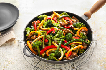Frying pan with tasty beef and vegetables on grunge background