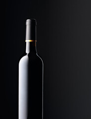 An unopened bottle of red wine on a black background.