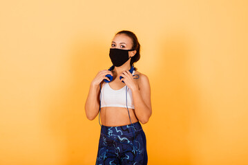 Portrait of fit african woman wearing face mask. Sporty woman in fitness wear standing on yellow background.