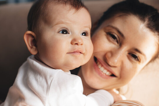 Close up photo of a freckled mother smiling proudly at camera holding her baby daughter