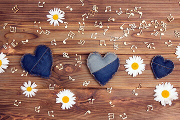 Denim hearts, chamomile flowers and musical notes on a wooden background.