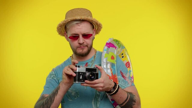 Photographer tourist taking photos on retro camera and smiling. Stylish bearded man in fashion t-shirt. Young guy on yellow studio background. People sincere emotions. Travel, summer holiday vacation